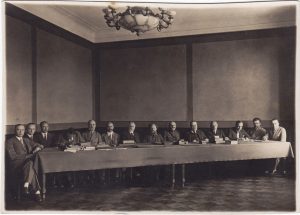Lietuvos Valstybės tarybos (1928–1940) nariai žinovai-bendradarbiai ir referentai posėdžio metu. Sėdi iš kairės į dešinę: dr. Vladas Juodeika, Zigmas Starkus, doc. Tadas Petkevičius, prof. Vladas Jurgutis, prof. Mykolas Römeris, gen. Petras Šniukšta, Valstybės tarybos pirmininkas Stasys Šilingas, prof. Antanas Kriščiukaitis, Liudvikas (Liudas) Ciplijauskas, Vincas Kalnietis, Boleslovas Masiulis, Vincas Nainys, Konstantinas Račkauskas, P. Morkus. Kaunas, 1928–1933 m. Trakų istorijos muziejus. Naudojimo teisės: CC BY. Nuotrauka iš Europeanos: https://bitly.cx/Tc15y.