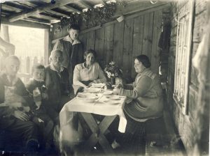 Prie stalo terasoje. Iš kairės: poetas Liudas Gira su katinu rankose, Vytautas Sirijos Gira su kačiukais, profesorius Eduardas Volteris, poetas Juazas Tysliava, Aleksandra Volterienė, Bronislava Girienė. Apie 1920 m. MLLM F 78. Maironio lietuvių literatūros muziejus. Naudojimo teisės: PD. Nuotrauka iš LIMIS