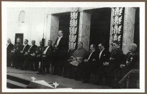 Iškilmingas Karininkų ramovės Kaune 1937 m. balandžio 23 d. atidarymas. Sėdi iš kairės: Kauno miesto burmistras Antanas Merkys, 2. Generalinio štabo viršininkas J. Česnys, 3. Žemės ūkio ministras Stasys Putvinskis, susisiekimo ministras Jokūbas Stanišauskas, krašto apsaugos ministras Stasys Dirmantas, Valstybės kontrolierius Konstantins Šakenis, mnistras pirmininkas Juozas Tūbelis, prezidentas Antanas Smetona, arkivyskupas J. Skvireckas, teisingumo ministras Stasys Šilingas, užsienio reikalų ministras Stasys Lozoraitis, vidaus reikalų ministras Julius Čaplikas, kariuomenės vadas Stasys Raštikis. 1937 m. ČDM Ip 1/2. Nacionalinis M. K. Čiurlionio dailės muziejus. Naudojimo teisės: CC BY-NC. Nuotrauka iš LIMIS