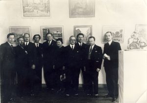 Dailės parodoje. Stovi iš kairės: profesorius Gudaitis; poetas Liudas Gira; latvių rašytojas Adolfas Erssas; poetas, dramaturgas Petras Vaičiūnas; Latvijos teatro direktorius Berzinis; Bronislava Girienė; Latvijos pasiuntinys Lietuvoje Robertas Liepinis (Liepinš); dailininkas Antanas Žmuidzinavičius; nežinomas asmuo; žurnalistas, politikas Justas Paleckis. 1936 m. MLLM F 73. Maironio lietuvių literatūros muziejus. Naudojimo teisės: PD. Nuotrauka iš LIMIS