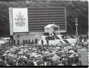 Edmundas Katinas. Popiežiaus Jono Pauliaus II vizitas Kaune. Popiežius Jonas Paulius II sėdi laikinai pastatytoje koplytėlėje S. Dariaus ir S. Girėno stadione. 1993 m. Kauno IX forto muziejus. Naudojimo teisės: CC BY-NC. Nuotrauka iš Europeanos