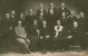 E. Lorson. Poetas V. Mykolaitis-Putinas tarp studijų draugų. Pirmoje eilėje iš kairės: Kazys Pakštas, M. Andziulytė-Ruginienė, Vincas Mykolaitis-Putinas, O. Vosyliūtė-Pakštienė, Edvardas Turauskas. Antroje eilėje iš kairės: nežinomas kunigas, Stasys Šalkauskis, U. Urniežiutė-Starkienė, Izidorius Tamošaitis, M. Ambraziejūtė-Kondrotienė, kunigas H. Žilevičius, O. Petrauskaitė-Krikščiūnienė, Pranas Jucaitis, kunigas J. Navickas. Viršuje: L. Bistras, V. Raulinaitis, K. Ruginis. 1918 m. Maironio lietuvių literatūros muziejus. Naudojimo teisės: PD. Nuotrauka iš Europeanos