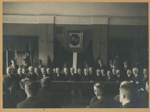 Ekonominės karių bendrovės fotoateljė. Iškilmingas posėdis Vytauto Didžiojo universitete. uotraukoje iš dešinės: Kazimieras Vasiliauskas, Petras Leonas, Blažiejus Čėsnys, Vladas Lašas, Zigmas Žemaitis, Vincas Krėvė-Mickevičius, Zigmas Kuzmickis, Pranas Jodelė, P. Čechavičius, Mykolas Römeris ir kt. XX a. 4 deš. LŠM III F 2921. Lietuvos švietimo muziejus. Naudojimo teisės: CC BY-NC-ND. Nuotrauka iš LIMIS