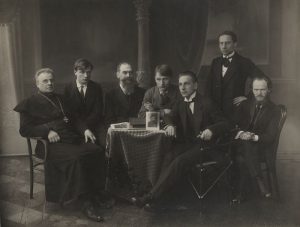 Lietuvių meno kūrėjų draugijos I-oji valdyba. Iš kairės: Jonas Mačiulis-Maironis, Paulius Galaunė, Juozas Naujalis, Balys Sruoga, Antanas Sutkus, Faustas Kirša ir Stasys Šilingas. 1920 m. Nacionalinis M. K. Čiurlionio dailės muziejus. Naudojimo teisės: PD. Nuotrauka iš Europeanos