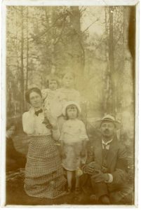 Šikšnių šeima (Iš kairės: sėdi Eugenija Paškevičiūtė (Smilgienė, 1886–19?), klūpo Liucija Paškevičiūtė-Šikšnienė (1881–1957) su dukra Elena ant peties, auklė, Marija Šikšnytė, Marcelinas Šikšnys). Druskininkai. 1914 m. Lietuvos nacionalinis dailės muziejus. Naudojimo teisės: PD. Nuotrauka iš Europeanos