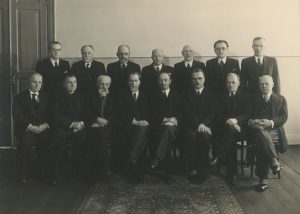 Boleslovas Savsenavičius. Vytauto Didžiojo universiteto profesoriai ir dėstytojai Kaune. Nuotraukoje iš kairės (sėdi): Kazimieras Vasiliauskas, Blažiejus Čėsnys?, Pranas Jodelė, Mykolas Biržiška, Stasys Šalkauskis (rektorius), Petras Šalčius, Antanas Purėnas, Augustinas Janulaitis; antroje eilėje: Vincas Mykolaitis-Putinas, Pranas Mažylis, Vaclovas Biržiška, Zigmas Žemaitis, Vladas Lašas, Zenonas Ivinskis, Petras Katilius. Apie 1939–1940 m. LŠM III F 2456. Lietuvos švietimo muziejus. Naudojimo teisės: CC BY-NC-ND. Nuotrauka iš LIMIS