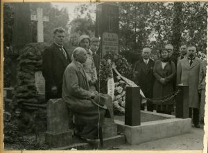 Prie Jono Basanavičiaus kapo (kairėje sėdi M. Šikšnys, dešinėje per vidurį stovi Konstantinas Stašys). Vilnius, Rasų kapinės. Lietuvos nacionalinis dailės muziejus. Naudojimo teisės: PD. Nuotrauka iš Europeanos