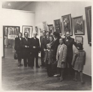 Dailininkai Rudens dailės parodos Kaune ekspozicijos salėje. Antras iš kairės stovi R. Kalpokas, toliau P. Rimša, A. Pancerovas, A. Žmuidzinavičius, D. Tarabildienė ir kiti. 1954 m. Nacionalinis M. K. Čiurlionio dailės muziejus. Naudojimo teisės: CC BY-NC-ND. Nuotrauka iš Europeanos