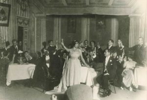 Scena iš Giuseppe’ės Verdi’io operos „Traviata“. Lietuvių meno kūrėjų draugijos operos vaidyklos atidarymas, 1920 metų gruodžio 31 diena. Centre Adelė Galaunienė – Violeta, Kipras Petrauskas – Alfredas Žermonas. Kauno miesto muziejus. Naudojimo teisės: PD. Nuotrauka iš Europeanos