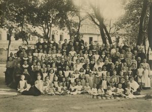 Aleksandra Jurašaitytė-Vailokaitienė. Didžiosios Vaikų prieglaudos auklėtiniai Vilniuje. Trečioje eilėje septinta iš kairės sėdi Emilija Vileišienė. 1917 m. ČDM ŽFp 4338. Nacionalinis M. K. Čiurlionio dailės muziejus. Naudojimo teisės: CC BY-NC. Nuotrauka iš LIMIS